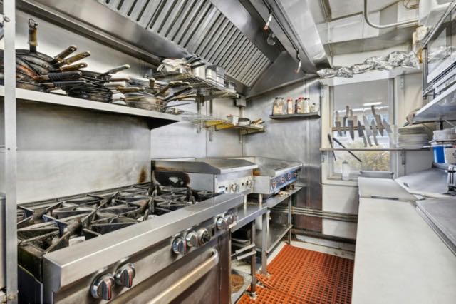 Cuisine professionnelle en inox avec fourneaux, plonge et étagères d’ustensiles
